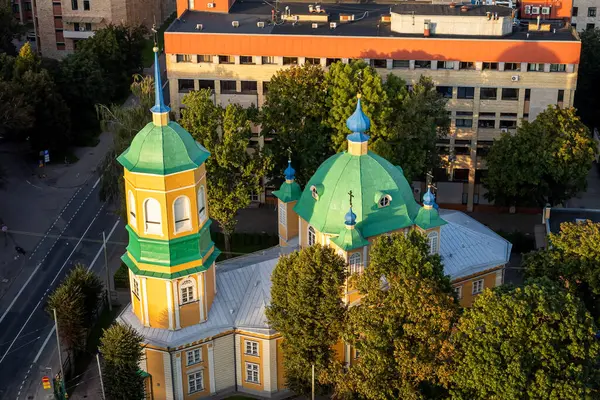 Şehir manzarasının üzerinde yükselen yeşil kilise kubbeleri, tarihi mimariyle çevresini çevreleyen modern çevreyi harmanlıyor. Sahne, şehir atmosferindeki kültürel mirası vurguluyor..