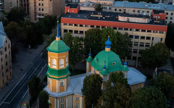 Şehir manzarasının üzerinde yükselen yeşil kilise kubbeleri, tarihi mimariyle çevresini çevreleyen modern çevreyi harmanlıyor. Sahne, şehir atmosferindeki kültürel mirası vurguluyor..