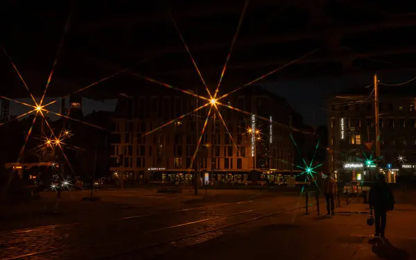 A dark cityscape at night, with streetlamp lights glowing like bright stars. The scene captures the quiet urban atmosphere.