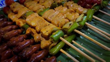 Izgara et çeşitleri. Sulu kızarmış et yeşil muz yapraklarında yatar. Kızarmış et parçaları şiş üzerinde.