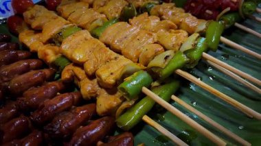 Izgara et çeşitleri. Sulu kızarmış et yeşil muz yapraklarında yatar. Kızarmış et parçaları şiş üzerinde.