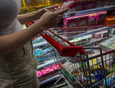 Yemek arabası ve süpermarkette. Kız satın almak için mal seçiyor. Bir araba dolusu yiyecek ve ev eşyası..