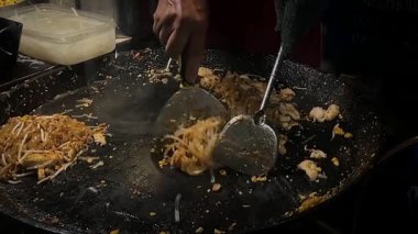 Tayland usulü kızarmış erişte pişirme işlemi. Şef, ısırık büyüklüğünde bir sokak yemeği yapmak için malzemeleri karıştırıyor.