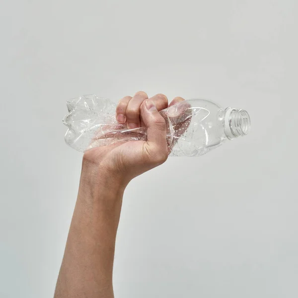 Partial male hand holding crumpled plastic bottle. Ecology safety and protection. Waste disposal and recycling. Environmental sustainability. Isolated on white background. Studio shoot. Copy space