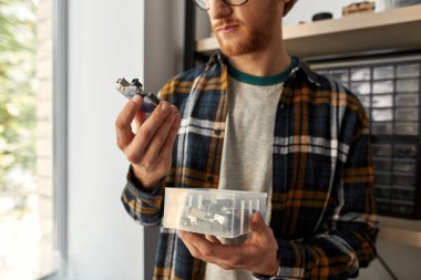 Kısmi erkek bilişim teknisyeni ya da mühendis güneşli ofisteki plastik kutudan mikroçipi tutuyor ve seçiyor. Gözlüklü genç adam. Modern dijital teknoloji ve yenilik geliştirme