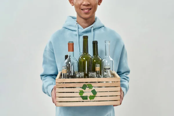 Obscure face of smiling man holding wooden box with empty glass bottles and jars. Ecology safety and protection. Waste disposal and recycling. Isolated on white background. Studio shoot. Copy space