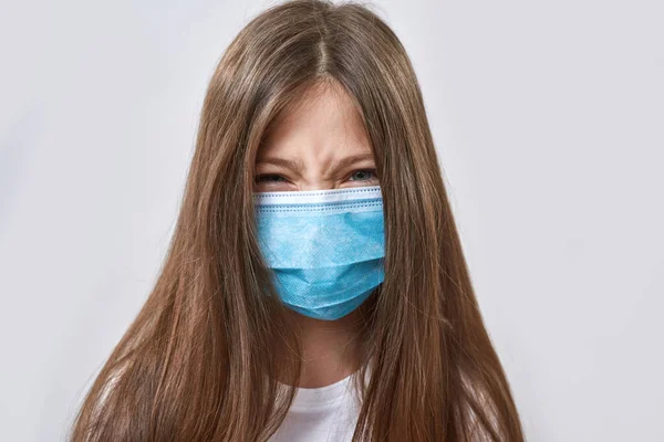 Angry caucasian little girl wearing medical mask looking at camera. Female child of zoomer generation. Health protection during COVID-19 epidemic. Isolated on white background. Studio shoot