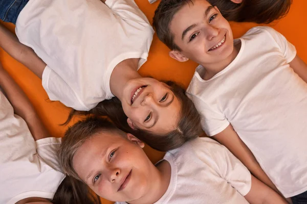 Cropped top view of smiling caucasian children looking at camera. Boys and girls of zoomer generation. Modern youngster lifestyle. Friendship. Isolated on orange background. Studio shoot