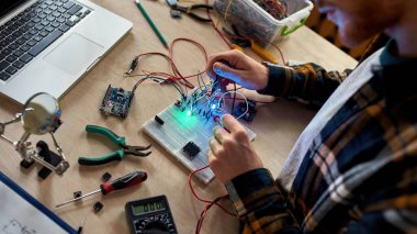 Kırpılmış erkek teknisyen ya da mühendis mikroçip ve voltmetreyle elektronik ekipmanlara kablo ve kablo bağlıyor. Adam masada bilimsel deney yapıyor. Modern teknoloji ve yenilik