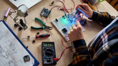 Mikroçip ve voltmetreyle elektronik ekipmanlara kablo ve kablo bağlayan kısmi erkek teknisyen veya mühendis. Adam masada bilimsel deney yapıyor. Modern teknoloji ve yenilik