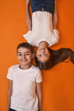 Kameraya gülümseyen beyaz kız ve oğlanın en iyi görüntüsü. Zoomer kuşağının çocukları. Modern genç yaşam tarzı. Arkadaşlık. Turuncu arka planda izole edilmiş. Stüdyo çekimi. Boşluğu kopyala
