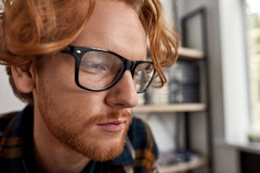 Teknik entrika izleyen kısmi kızıl saçlı beyaz adamın yüzünü kapatın. Zeki yakışıklı entelektüel erkek gözlük takıyor. Bulanık ofiste bilişim programcısı, teknisyeni veya mühendisi