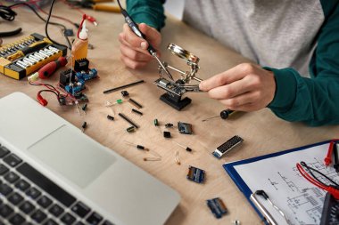 Kısmi erkek teknisyen ya da mühendis mikroçipi lehimleyen lehimleme demiriyle büyüteç altında dizüstü bilgisayarı, teknik düzeni, aletleri ve bileşenleri olan bir masada. Modern teknoloji ve yenilik