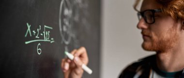 Kafkasyalı kısmi genç adam bulanık seyirci ya da sınıflarda tahtaya kalemle teknik ya da matematik formülü yazıyor. IT, teknik ve mühendislik eğitimi. Okul, üniversite, enstitü, üniversite