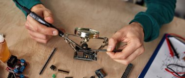 Kırpılmış erkek teknisyen ya da mühendis mikroçip lehimleme demiri çeşitli teknik bileşenlerle büyüteç altında masada. Modern teknoloji ve yenilik