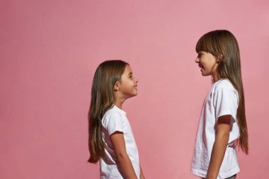 Gülümseyen beyaz kızların yan görünüşü. Birbirlerine bakıyorlar. Zoomer kuşağının kız arkadaşları. Modern genç yaşam tarzı. Arkadaşlık. Pembe arka planda izole edilmiş. Stüdyo çekimi. Boşluğu kopyala