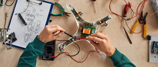 Kısmi erkek bilişim teknisyeni ya da mühendisinin masadaki parçalanmış insansız hava aracını çeşitli teknik aletler ve parçalarla kontrol edişinin üst görüntüsü. Modern teknoloji ve yenilik