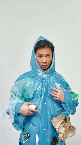 様々なゴミでいっぱいのレインコートを着たアジア人男性 生態系の安全と保護 廃棄物処理とリサイクル 環境の持続可能性 白い背景に隔離されている スタジオ撮影 スペースのコピー — ストック写真