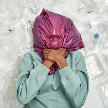 Siyah bir kız plastik çöpler arasında kafasında torba ile boğuluyor. Ekoloji güvenliği ve korunma. Çöp öğütücü ve geri dönüşüm. Çevresel sürdürülebilirlik. Beyaz arka planda izole edilmiş. Stüdyo çekimi
