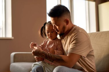 Baba ve kızı evdeki dijital termometreyi kontrol ediyorlar. Asyalı bir adam ve küçük bir kız. Sağlık ve tıbbi bakım. Aile ilişkisi. Ebeveynlik ve babalık. Modern yerli yaşam tarzı