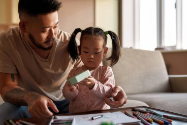 Baba, evde çizim yaparken kızına bak. Asyalı bir adam ve küçük bir kız birlikte vakit geçiriyorlar. Ev eğlencesi ve eğlence. Aile ilişkisi. Ebeveynlik ve babalık