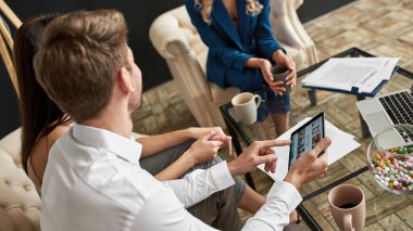 Çift arkası dijital tablette dinlenmek için yer seçiyor. Seyahat acentesinde kısmi bayan turist temsilcisi de var. Hizmet ve müşterilerle iletişim. Tatil, turizm, hafta sonu ve yolculuk