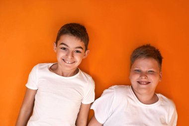 Kameraya gülümseyen beyaz çocukların en üst görüntüsü. Zoomer kuşağının erkek çocukları. Modern genç yaşam tarzı. Arkadaşlık. Turuncu arka planda izole edilmiş. Stüdyo çekimi. Boşluğu kopyala