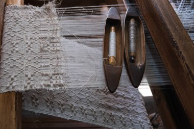 Eski bir dokuma tezgahının, beyaz ipliklerin ve eski ahşap bir mekiğin yakın çekimi. El dokuması.