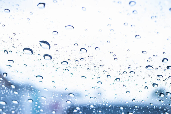 Rain drop texture on car glass against blue background.