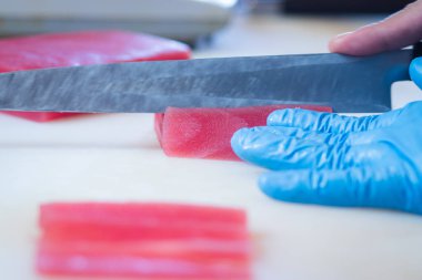 Taze ton balığı filetosu kesen mavi eldivenli bir şefin elleri Japon ton balıklı sashimi yapımında kullanılır..