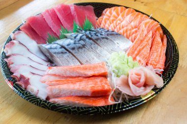 Japon desenli tepside çeşit çeşit saşimi. Taze ton balığı, taze somon, taco dokunaçları, yengeç çubukları ve uskumru, wasabi ve zencefil turşusuyla süslenmiş..