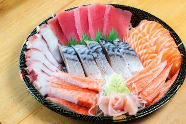 Japon desenli tepside çeşit çeşit saşimi. Taze ton balığı, taze somon, taco dokunaçları, yengeç çubukları ve uskumru, wasabi ve zencefil turşusuyla süslenmiş..