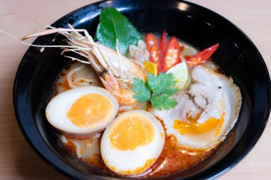 Tom Yum Ramen üzerine chashu domuz eti, soya soslu yumurta turşusu, nehir karidesi ve Tom yum baharatları. Tom Yum Ramen, Taylandlı Tom Yum ile birleşerek lezzetli bir tat veren Japon usulü bir eriştedir..