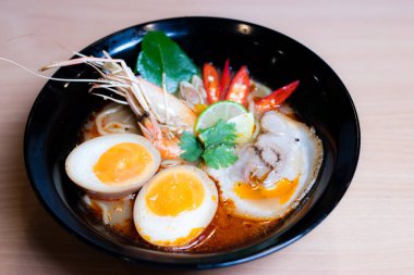 Tom Yum Ramen üzerine chashu domuz eti, soya soslu yumurta turşusu, nehir karidesi ve Tom yum baharatları. Tom Yum Ramen, Taylandlı Tom Yum ile birleşerek lezzetli bir tat veren Japon usulü bir eriştedir..