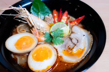 Tom Yum Ramen üzerine chashu domuz eti, soya soslu yumurta turşusu, nehir karidesi ve Tom yum baharatları. Tom Yum Ramen, Taylandlı Tom Yum ile birleşerek lezzetli bir tat veren Japon usulü bir eriştedir..