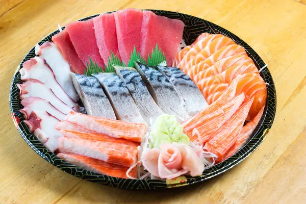 stock image Assorted sashimi on a Japanese patterned tray. It consisted of fresh tuna, fresh salmon, taco tentacles, crab sticks and mackerel, garnished with wasabi and pickled ginger.