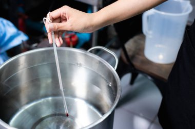 Kaynayan suyun sıcaklığını ölçmek için termometreyi tutan bir el..