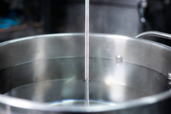 A hand holding a thermometer to measure the temperature of the water being boiled.