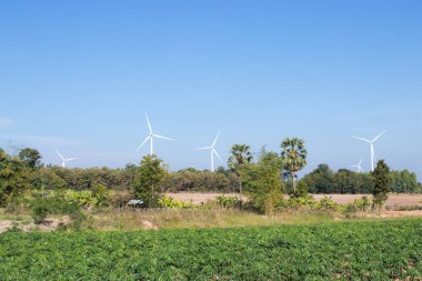 Elektrik üretmek için kullanılan bir rüzgar türbini mavi gökyüzü arka planındaki yeşil bir alanda bulunmaktadır..