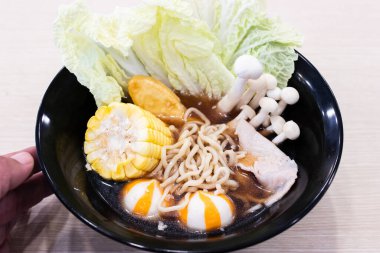 Siyah bir kasede erişte çorbası. Kıvırcık erişte çorbası, tatlı mısır, gevrek napa lahana yaprakları, taze domuz eti dilimleri, altın balık tofu, zıplayan portakal ve beyaz balık topları ve taze beyaz shimeji mushroo kümesi.