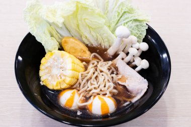 Siyah bir kasede erişte çorbası. Kıvırcık erişte çorbası, tatlı mısır, gevrek napa lahana yaprakları, taze domuz eti dilimleri, altın balık tofu, zıplayan portakal ve beyaz balık topları ve taze beyaz shimeji mushroo kümesi.