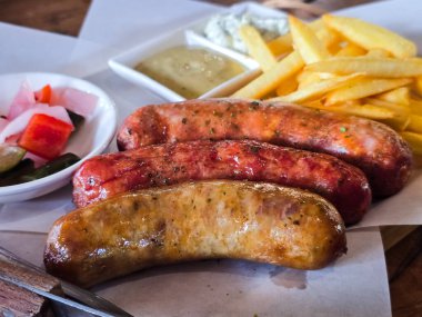 Patates kızartması, hardal sosu ve sebze turşusuyla servis edilen ızgara sosisler. Lezzetli ve doyurucu bir yemek. Rahatlatıcı yemek severler için mükemmel..