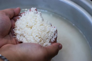 Elleri yakın plan, ıslanmış glutinous pilavını bir tencere suyun üstünde tutarak pişirmeye hazırlanıyor. Geleneksel bir yemek hazırlama süreci Asya mutfağında ve yapışkan pirinç yemeklerinde yaygındır..