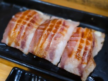 Izgara pastırmalı suşi, siyah tepside servis ediliyor. Sulu dokuyu, parlak sosu ve baharatlı Japon füzyon stili sunumunu vurgulayan yakın plan görüntü.