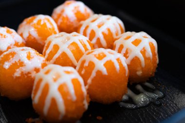 Parlak turuncu tobiko kaplı suşi topları ve siyah tepside beyaz mayonez serpiştirilmiş, dokuyu ve canlı rengi renklendiriyor..