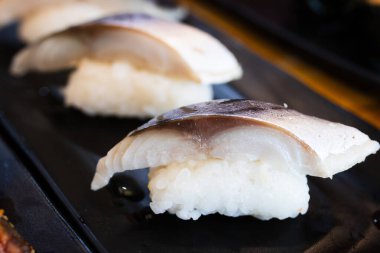Sirkeli pirincin üstünde ızgara uskumru dilimli Saba nigiri suşisi Japon restoranında siyah bir tabakta servis edilir..