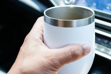 Arabanın içinde paslanmaz çelik bir bardak tutan, seyahat ve içecek yaşam tarzını gösteren bir el..