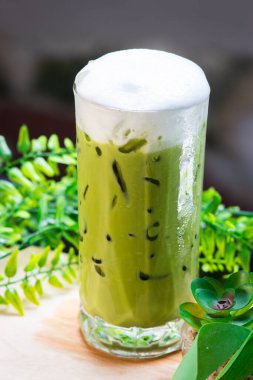 Yeşil yapraklarla çevrili, kremalı süt köpüğüyle kaplı buzlu kibrit yeşil çay, ferahlatıcı ve soğuk..