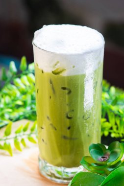 Yeşil yapraklarla çevrili, kremalı süt köpüğüyle kaplı buzlu kibrit yeşil çay, ferahlatıcı ve soğuk..