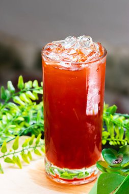 Buzla dolu bir bardak buzlu Thai çayı, arka planda yeşil yapraklarla ahşap bir yüzeye yerleştirilmiş, soğuk ve ferahlatıcı..